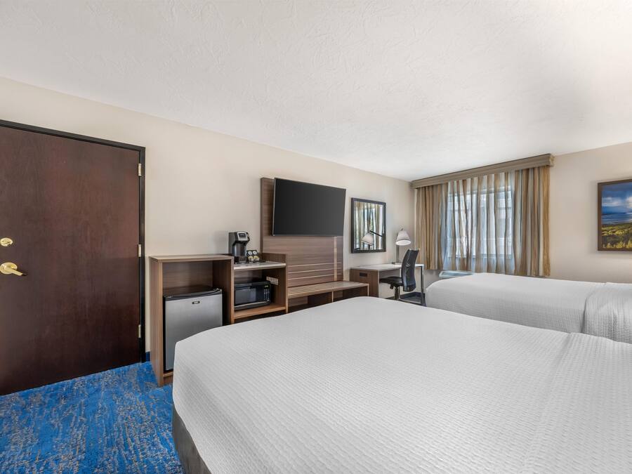 A hotel room with two beds, a desk, a television, and a window with curtains.
