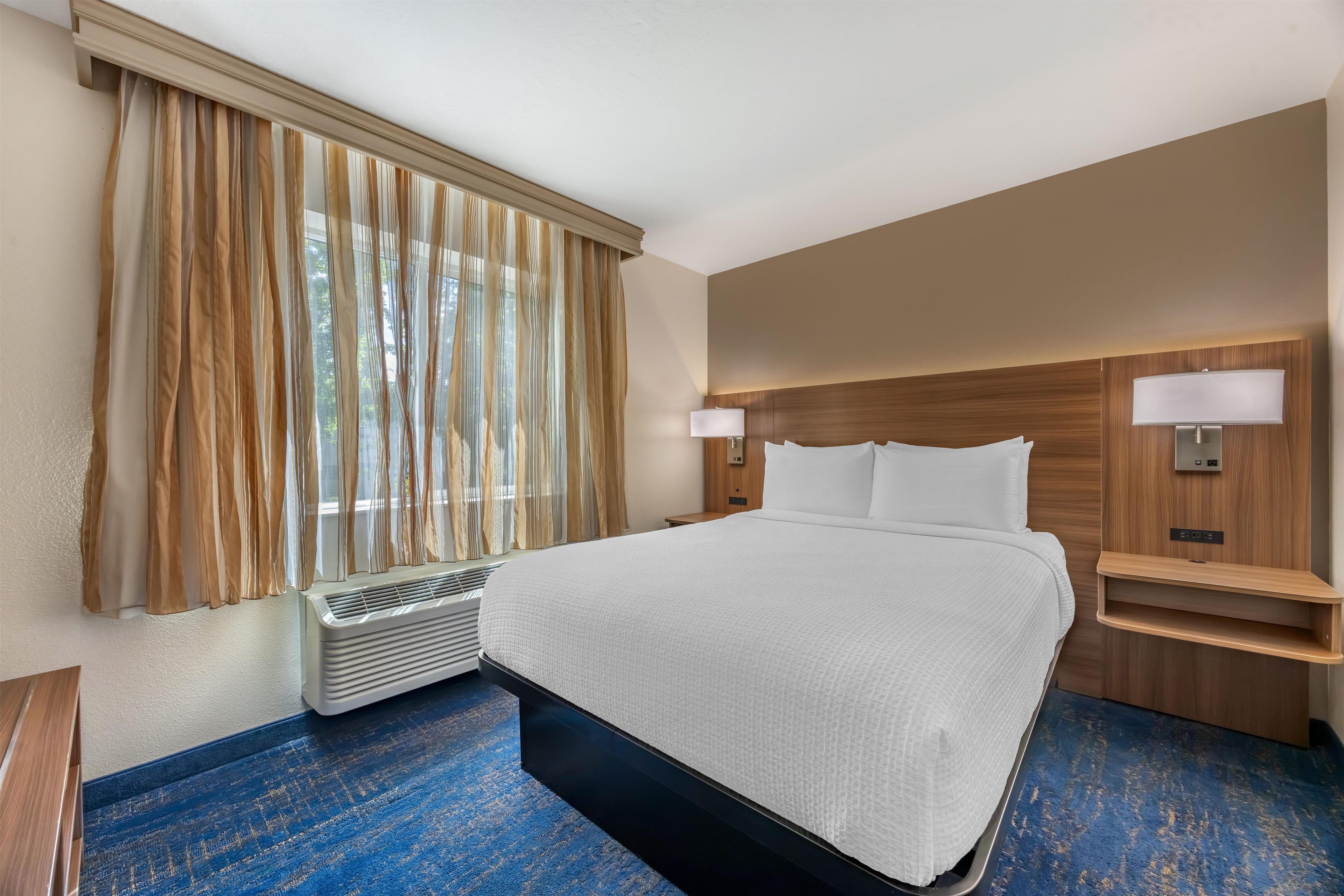 A hotel room with a large bed, bedside lamps, a nightstand, and a window with curtains.