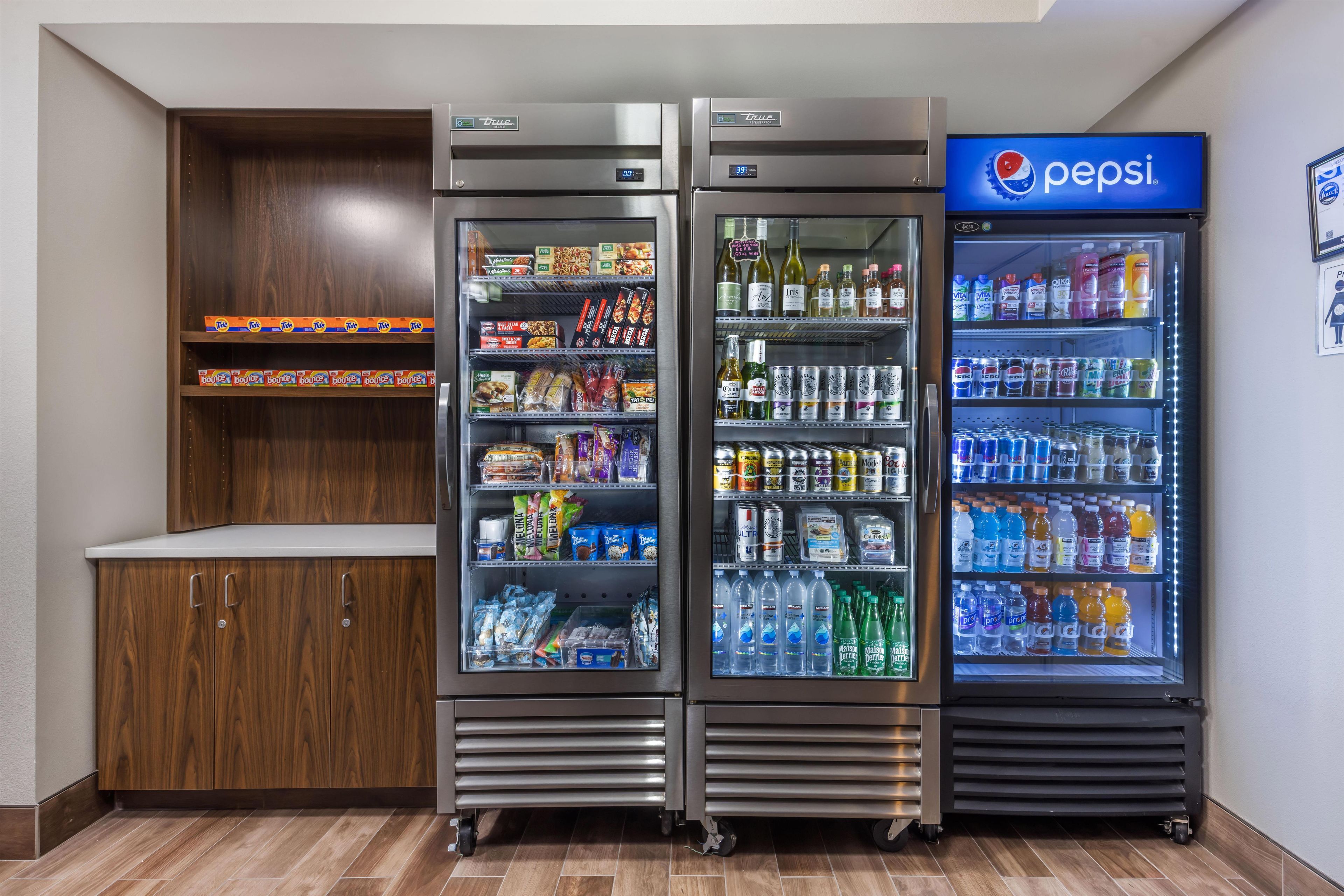 A vending machine area with a Pepsi refrigerator and a True refrigerator, both stocked with various food and drink items.