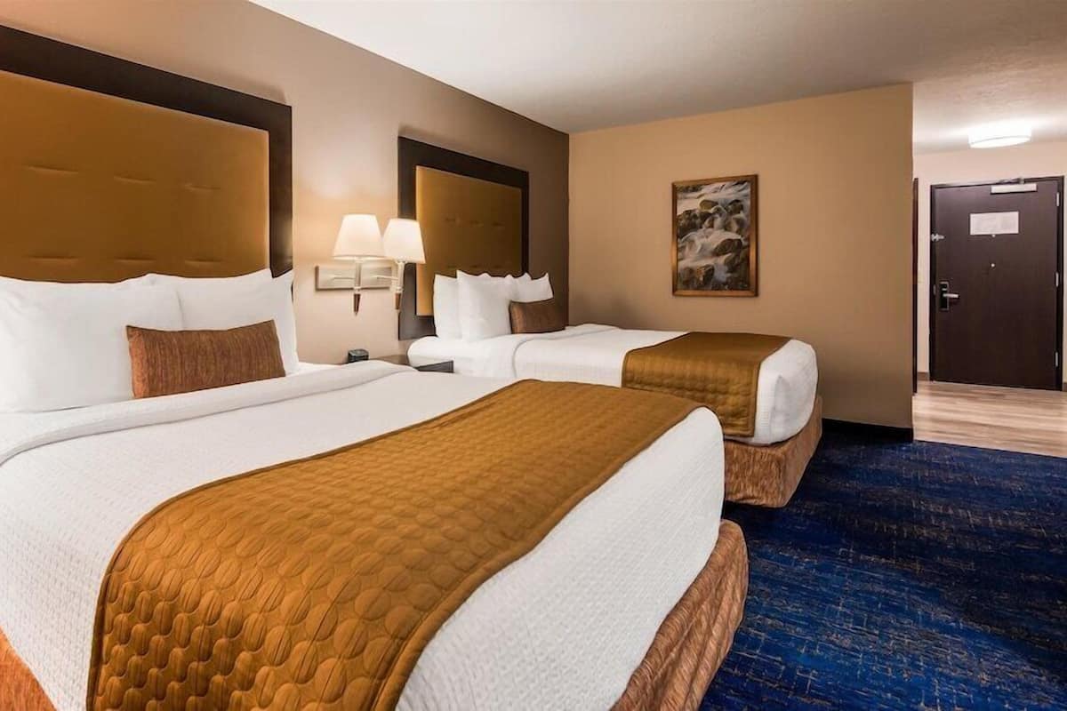 Une chambre d’hôtel avec deux lits, une grande tête de lit, un tableau au mur et une porte.