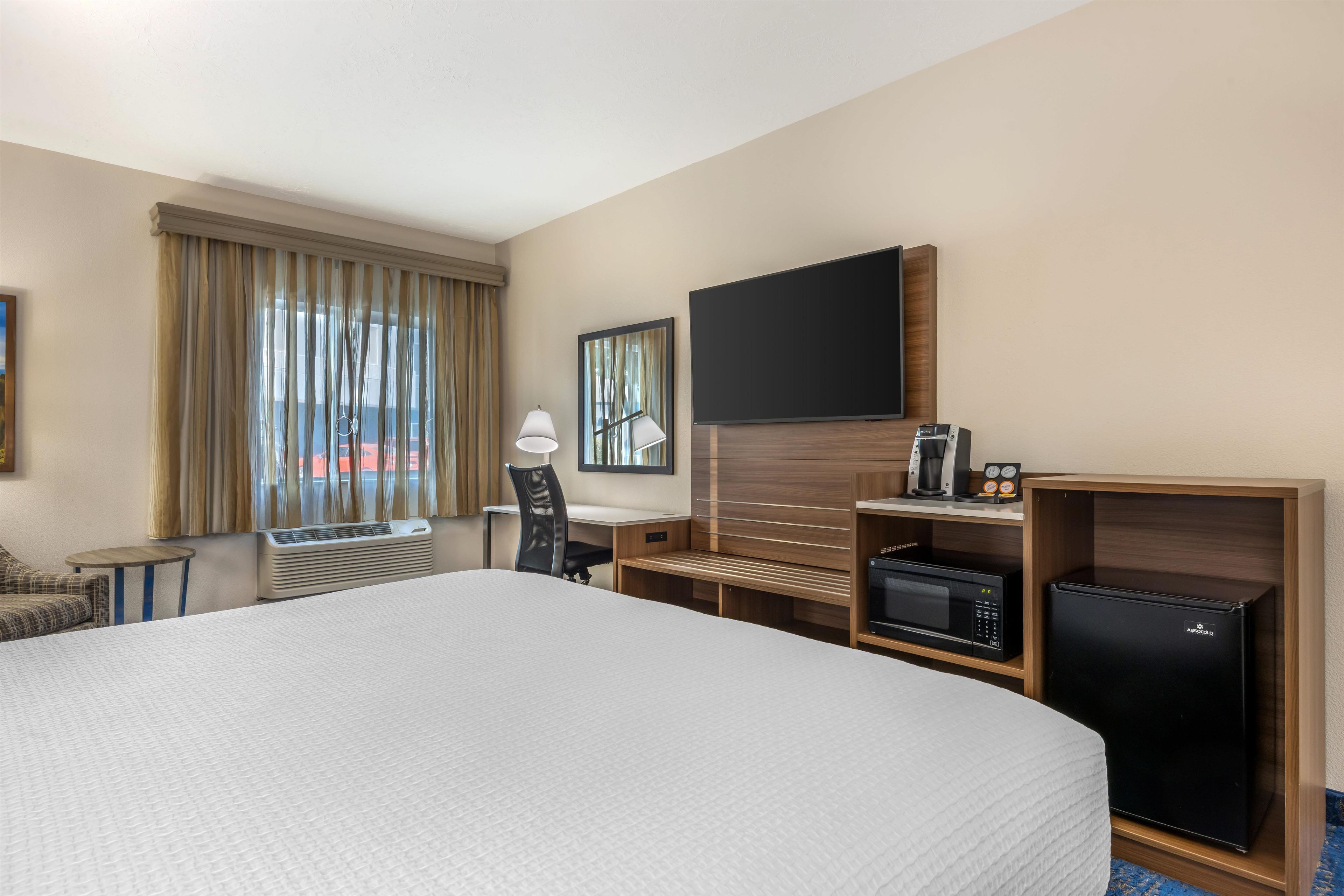 A hotel room with a large bed, a desk, a chair, a flat-screen TV, a coffee maker, a microwave, and a mini-fridge.
