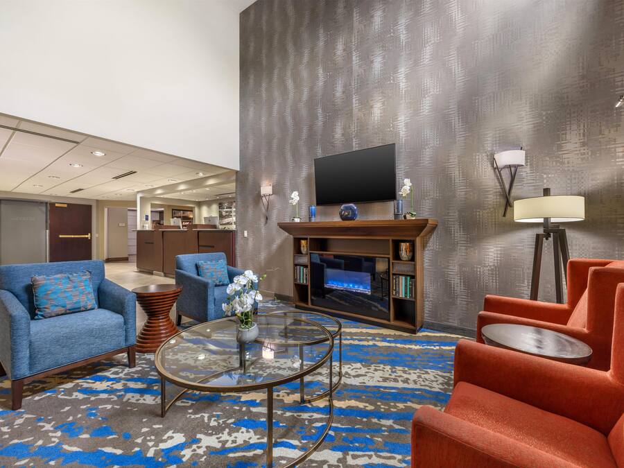 A modern hotel lobby with a fireplace, seating area, and a flat-screen TV.