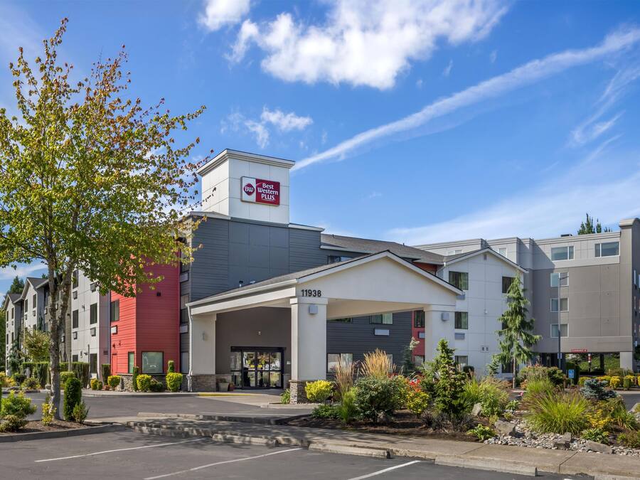 A hotel with a modern design, featuring a prominent Best Western PLUS sign, a covered entrance, and a parking lot with a clear sky in the background.