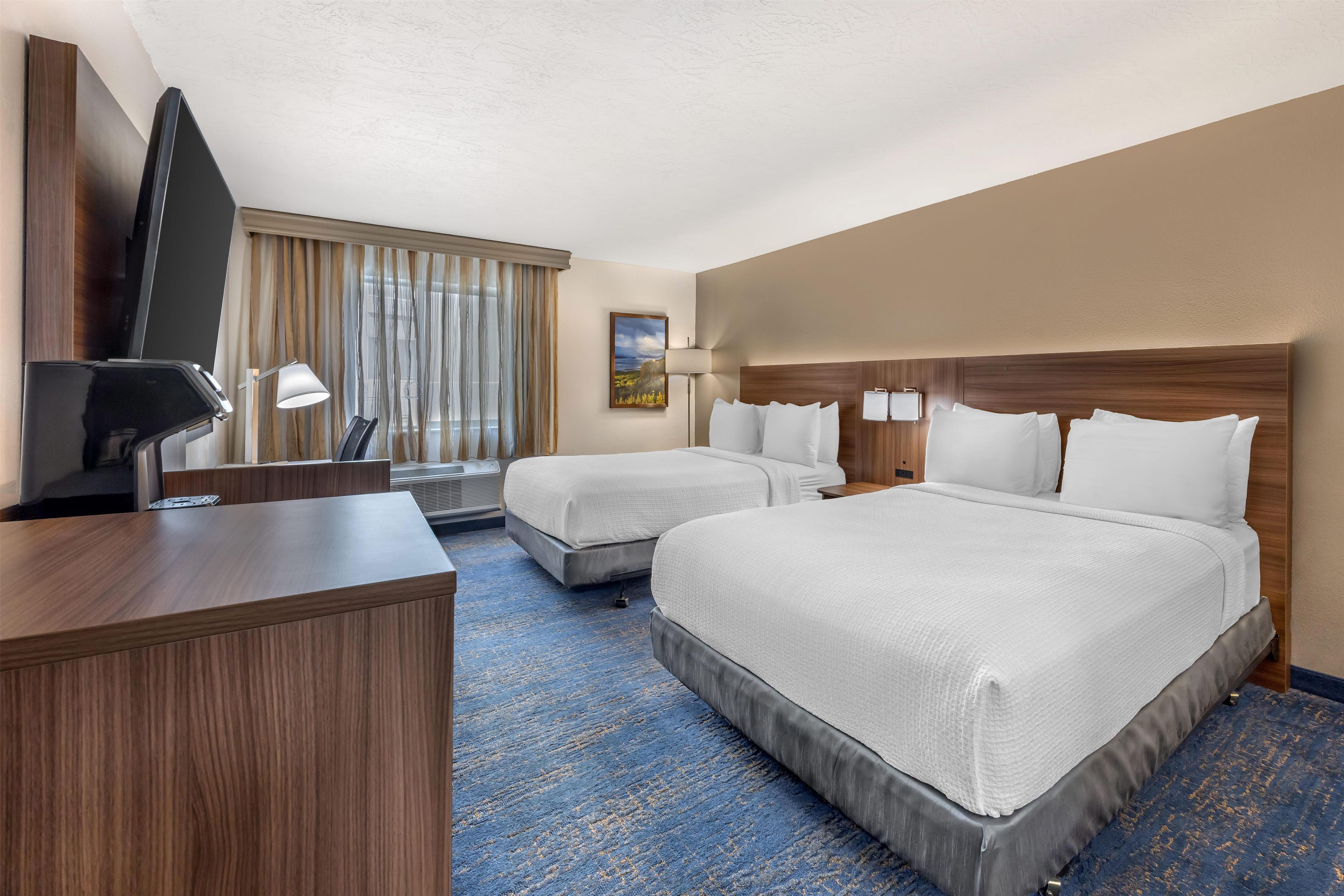 A hotel room with two beds, a desk, a TV, and a painting on the wall.