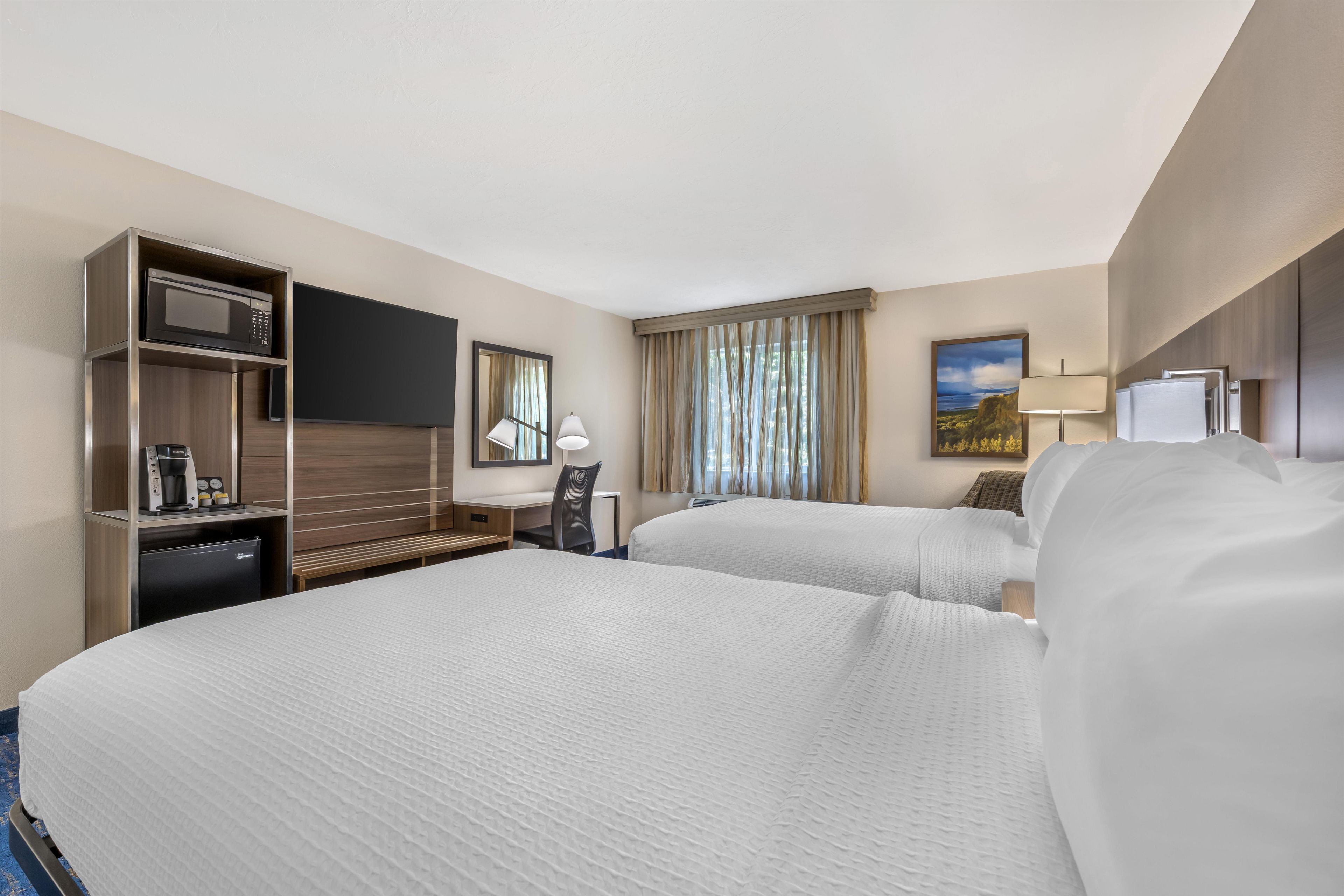 A hotel room with two beds, a desk with a microwave, a coffee maker, and a TV.