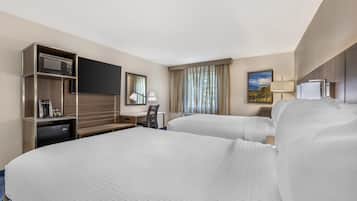 A hotel room with two beds, a desk with a microwave, a coffee maker, and a TV.