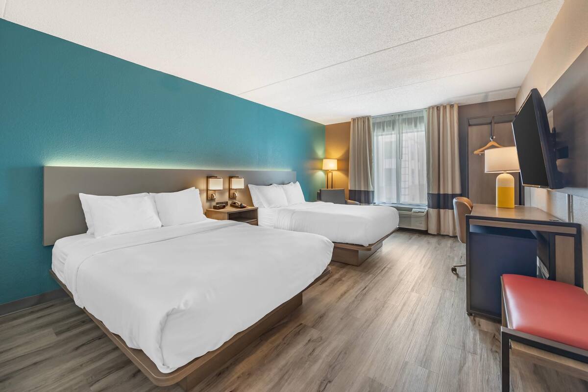 A hotel room with two beds, a desk, a chair, and a TV.