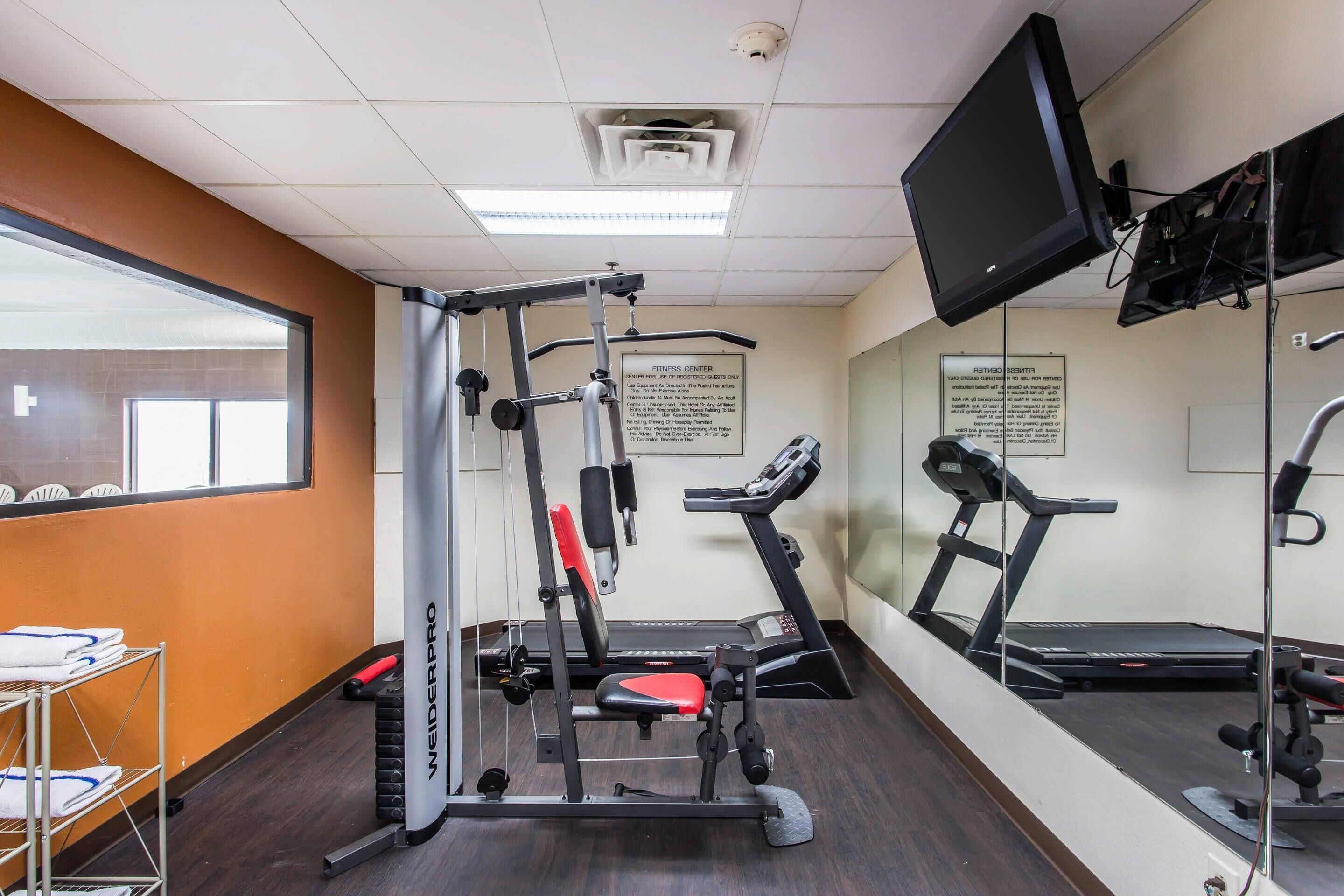 A fitness center with a treadmill, weight bench, and mirrored walls.