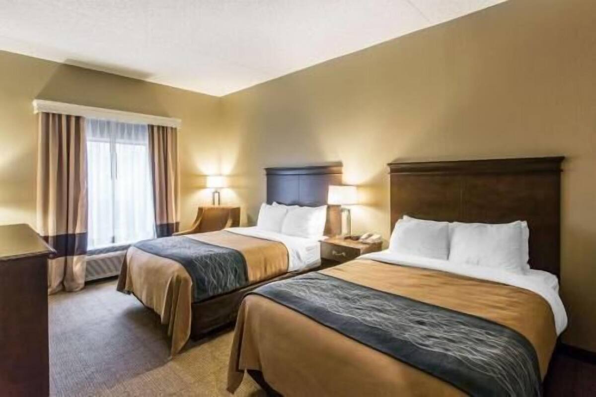 A hotel room with two beds, a window with curtains, a desk, and a lamp.