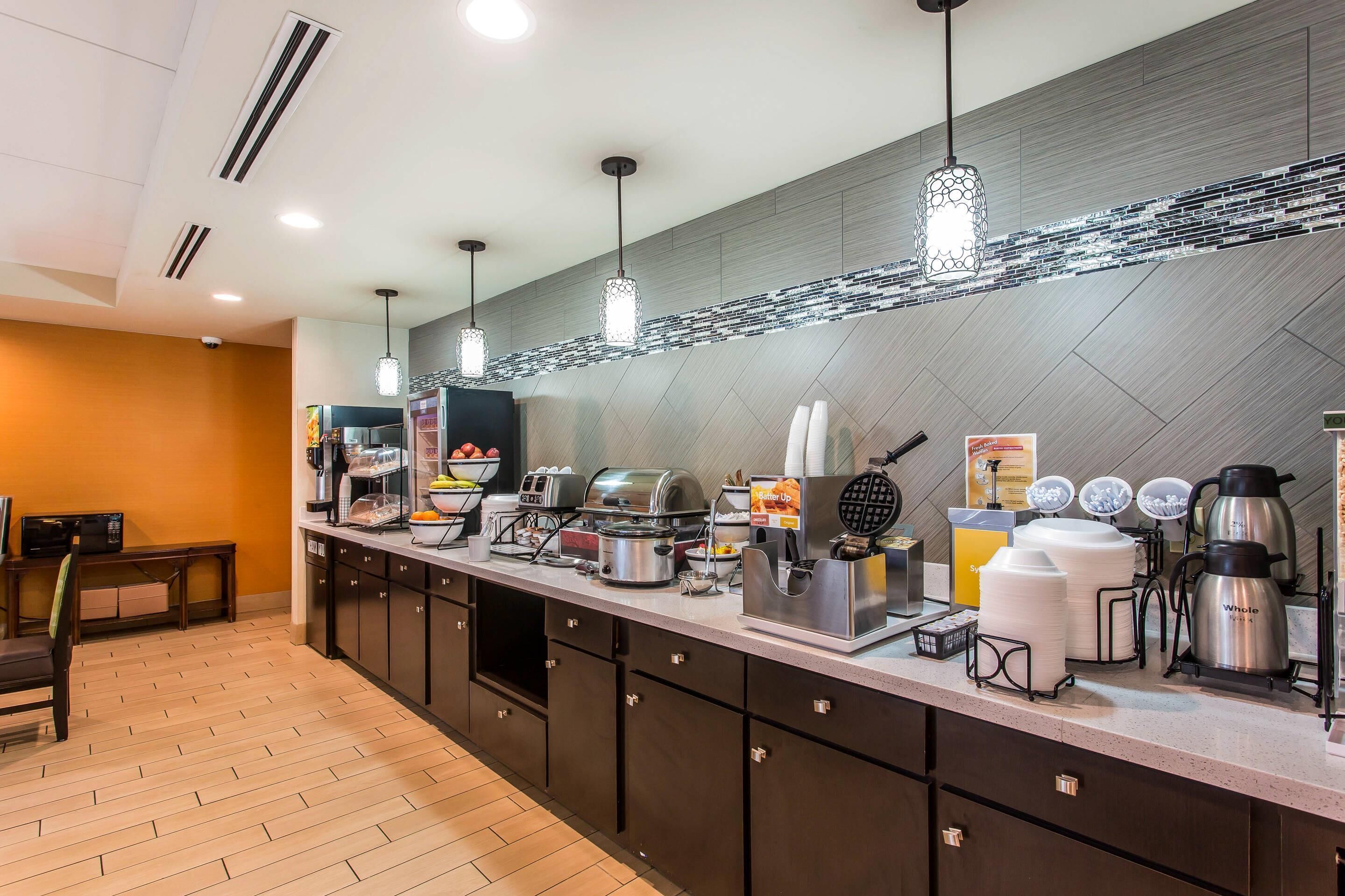 A modern kitchen area with a long counter, various appliances, and hanging pendant lights.