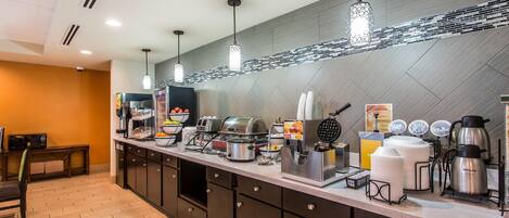 A modern kitchen area with a long counter, various appliances, and hanging pendant lights.