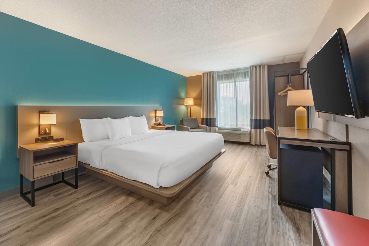 A hotel room with a bed, bedside tables, a desk, a chair, a TV, and a window with curtains.