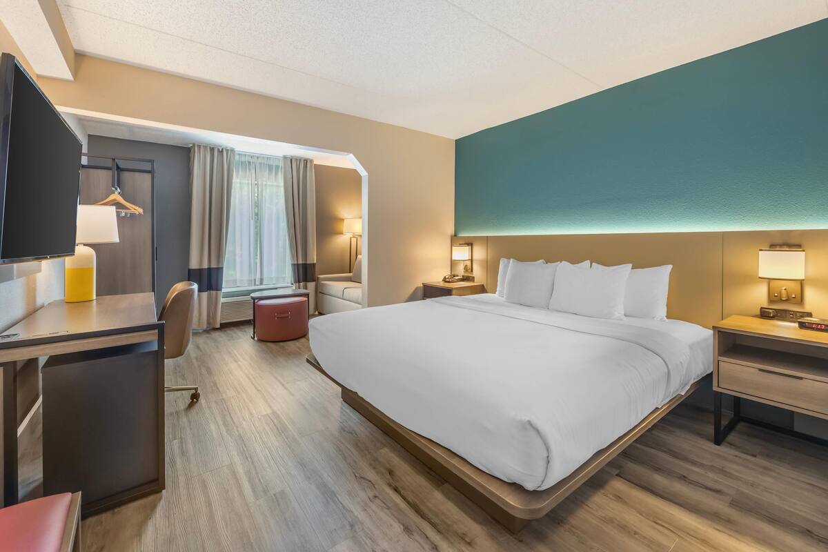 A hotel room with a large bed, a desk, a chair, a TV, and a window with curtains.