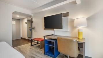 Quarto de hotel com cama, escrivaninha, cadeira, televisão e abajur.