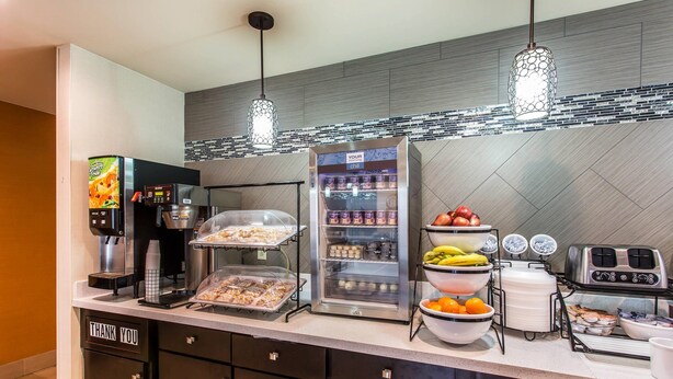 Una barra de desayuno con una máquina de café, un refrigerador, cuencos de fruta y un tostador.
