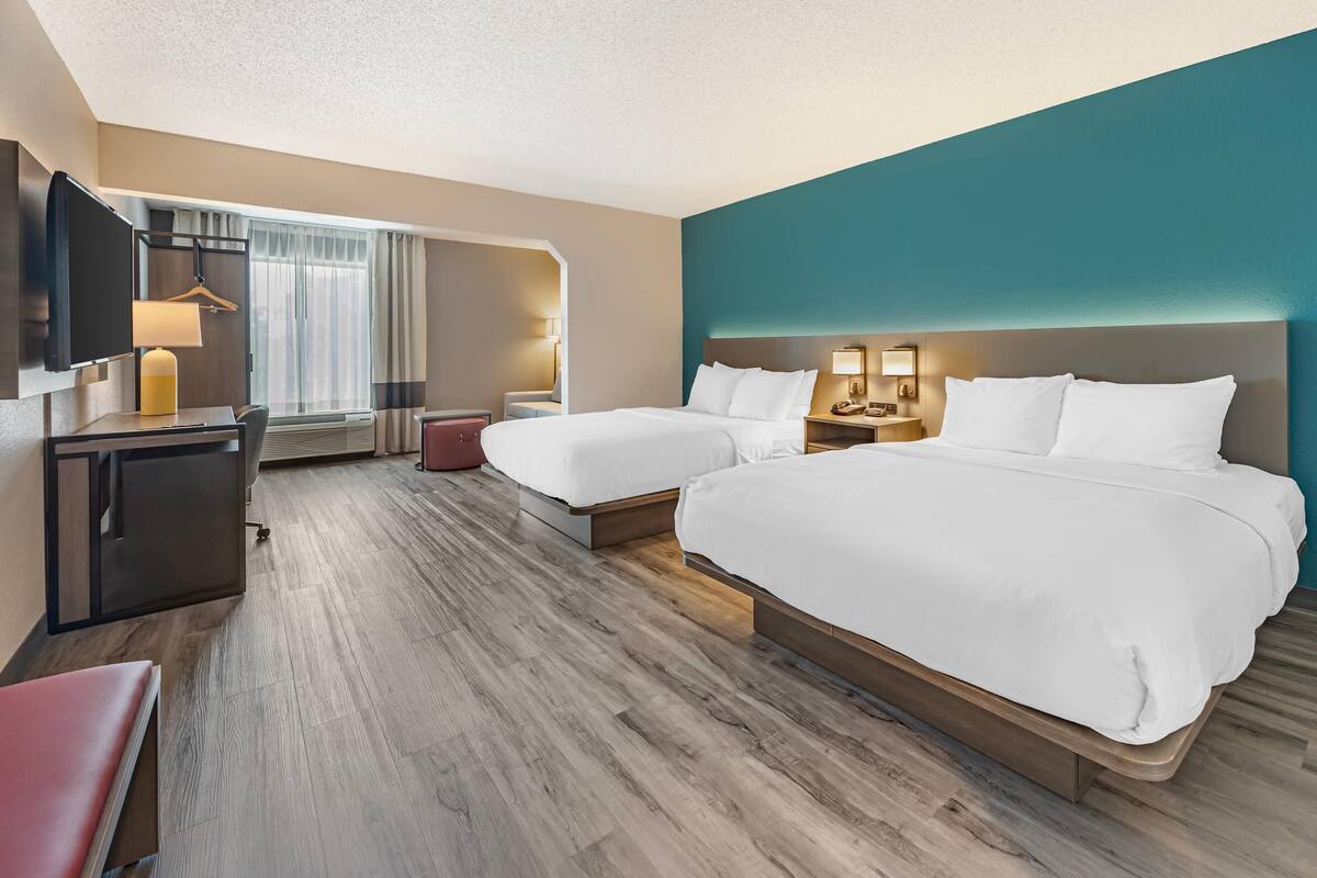 A hotel room with two beds, a desk, a TV, and a seating area.