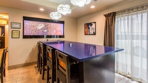 Una cocina moderna con una isla central, luces colgantes, un amplio ventanal con cortinas y obras de arte enmarcadas en las paredes.
