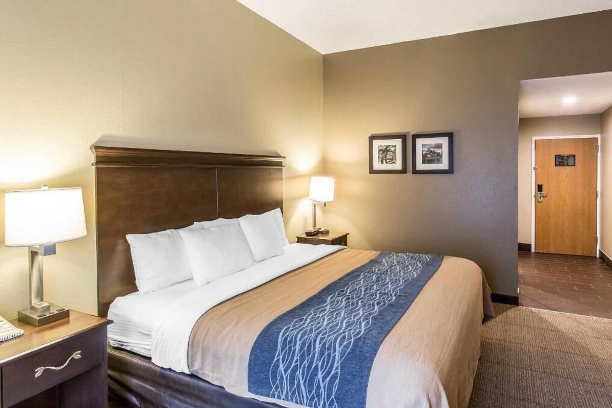 A hotel room with a bed, bedside lamps, a nightstand, and a door.