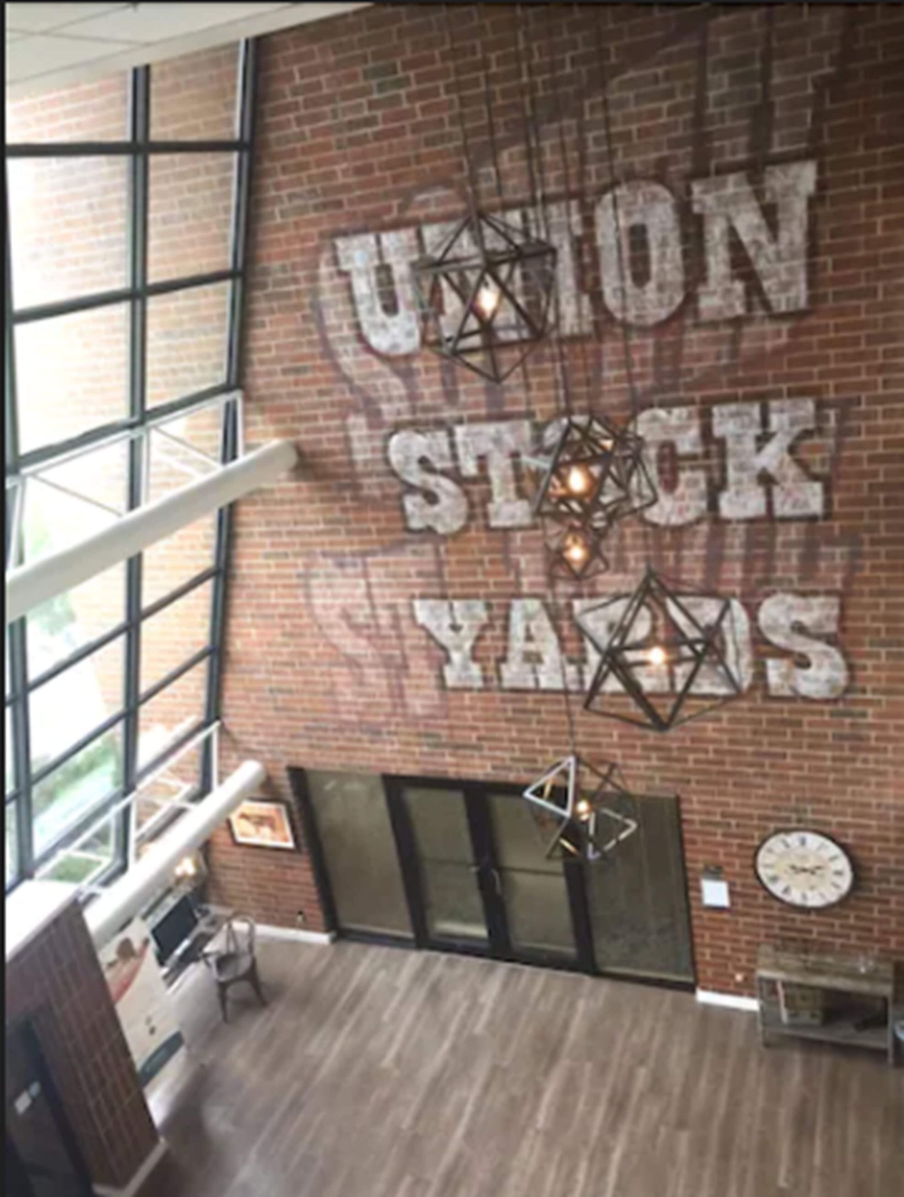Eine großzügige Lobby mit einer großen Ziegelwand, einem Schild mit der Aufschrift "Union Stock Yards" und modernen Leuchten.