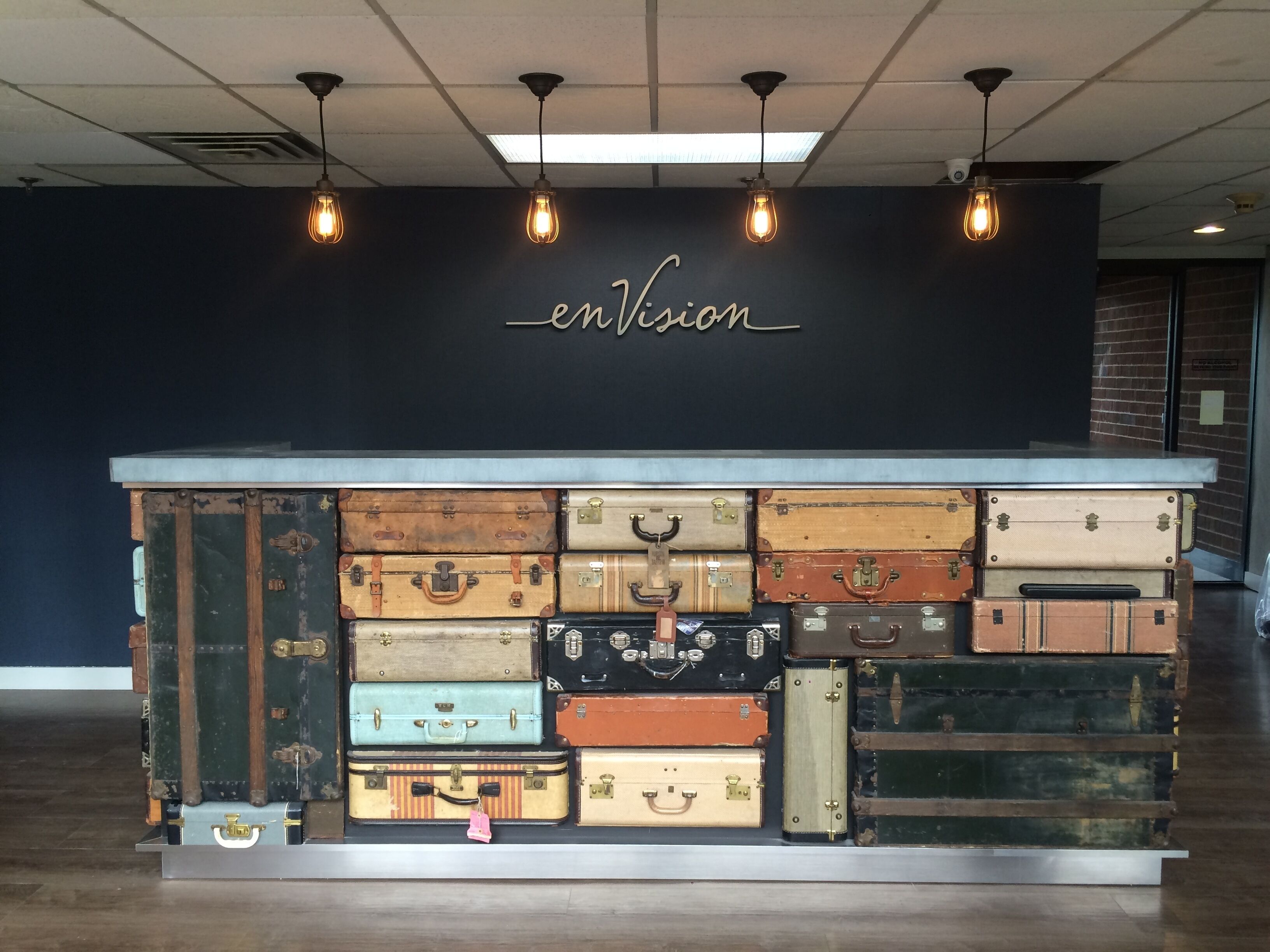 A display of vintage suitcases stacked on a counter with a sign reading "enVision" above.