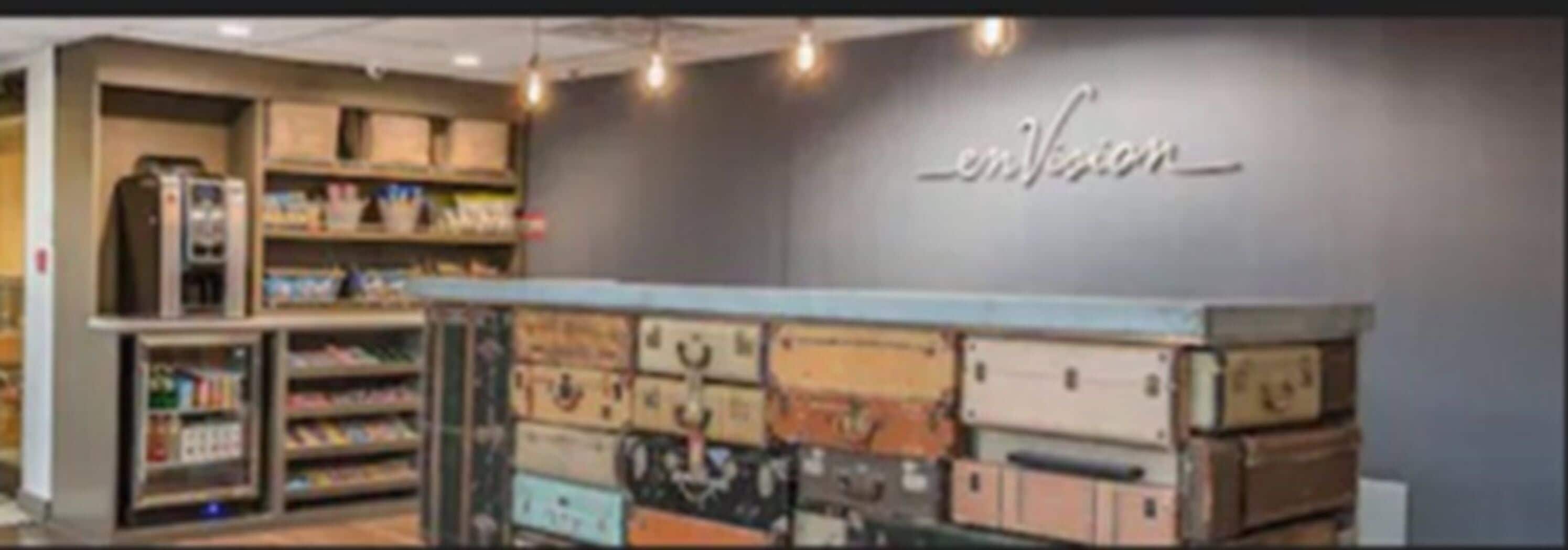 A store interior with shelves stocked with various items, a counter with suitcases, and a wall with the word 'envision' displayed.