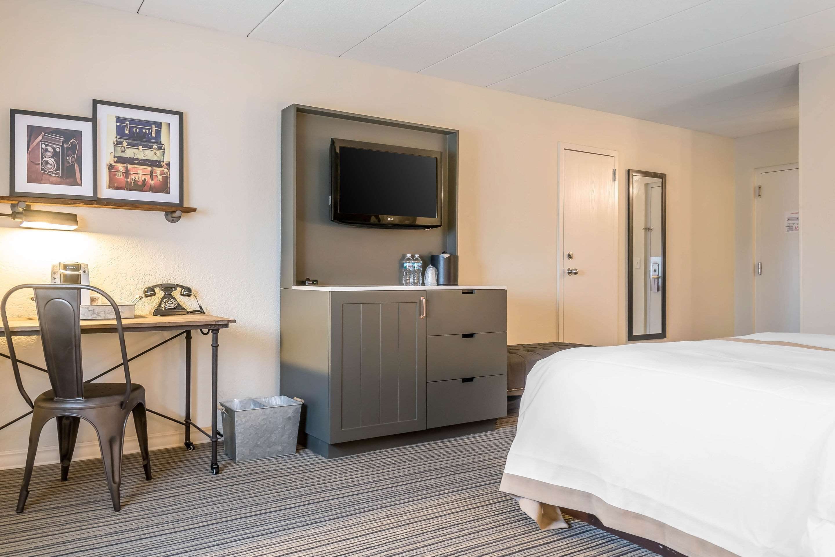 A hotel room with a bed, a desk with a chair, a television, and a minibar.