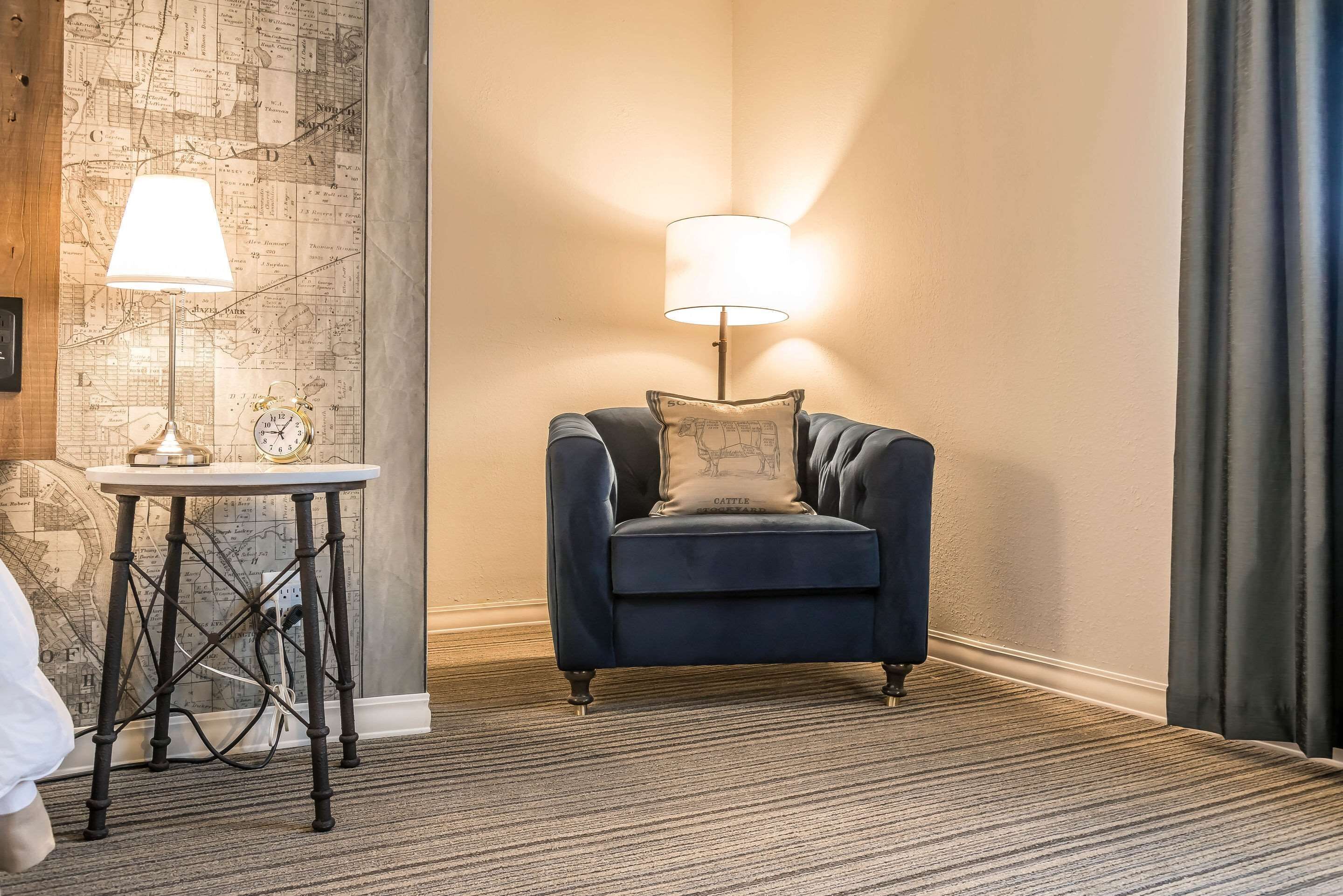 A room with a blue armchair, a small table with a lamp, and a map on the wall.