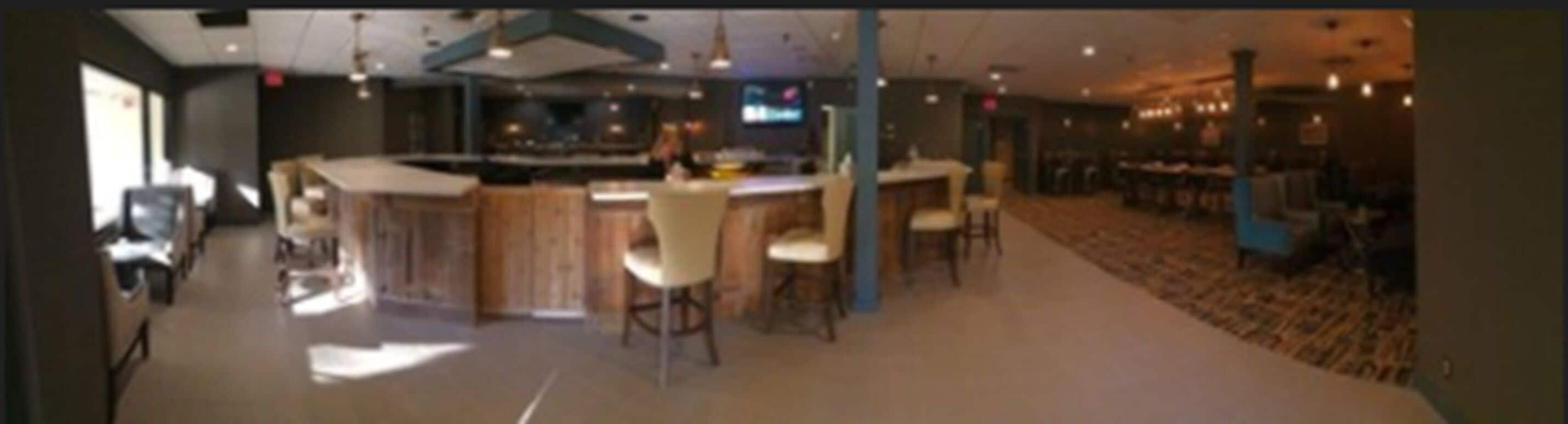A modern bar area with a counter, bar stools, and a television screen.