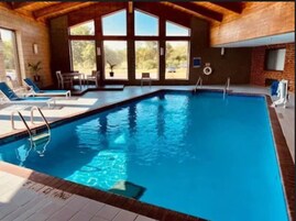 Una piscina interior rectangular con agua azul cristalina, rodeada de sillas de descanso y un techo de madera.