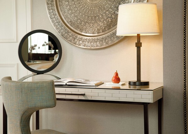 A room with a round mirror, a table with a lamp, a chair, and a decorative plate. - Lansdowne Resort and Spa (Leesburg)