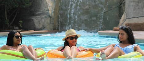Three individuals in a swimming pool with a waterfall feature in the background.