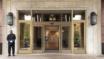 A hotel entrance with a double door, a stone facade, and a uniformed attendant.
