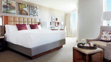 A hotel room with a large bed, a side table, a chair, and artwork on the walls.