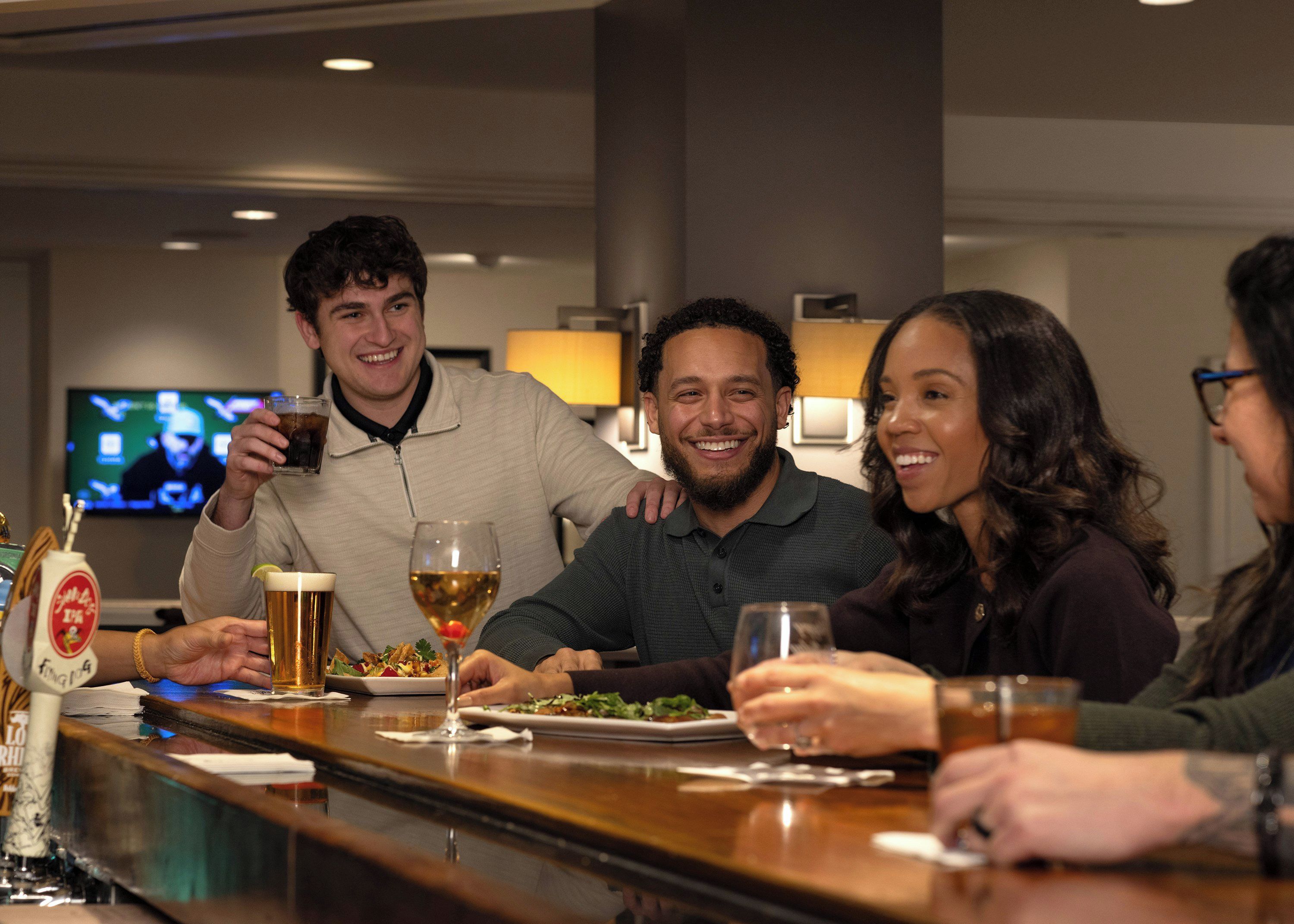 Un grupo de personas sentadas en un bar, con bebidas y un televisor al fondo.