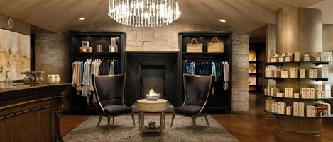 A hotel lobby with a fireplace, two armchairs, a chandelier, and a display of toiletries.