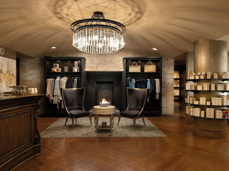 A hotel lobby with a fireplace, two armchairs, a chandelier, and a display of toiletries.