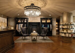 A hotel lobby with a fireplace, two armchairs, a chandelier, and a display of toiletries. - Lansdowne Resort and Spa (Leesburg)