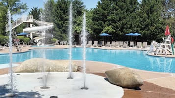 A swimming pool with water features, lounge chairs, and umbrellas.