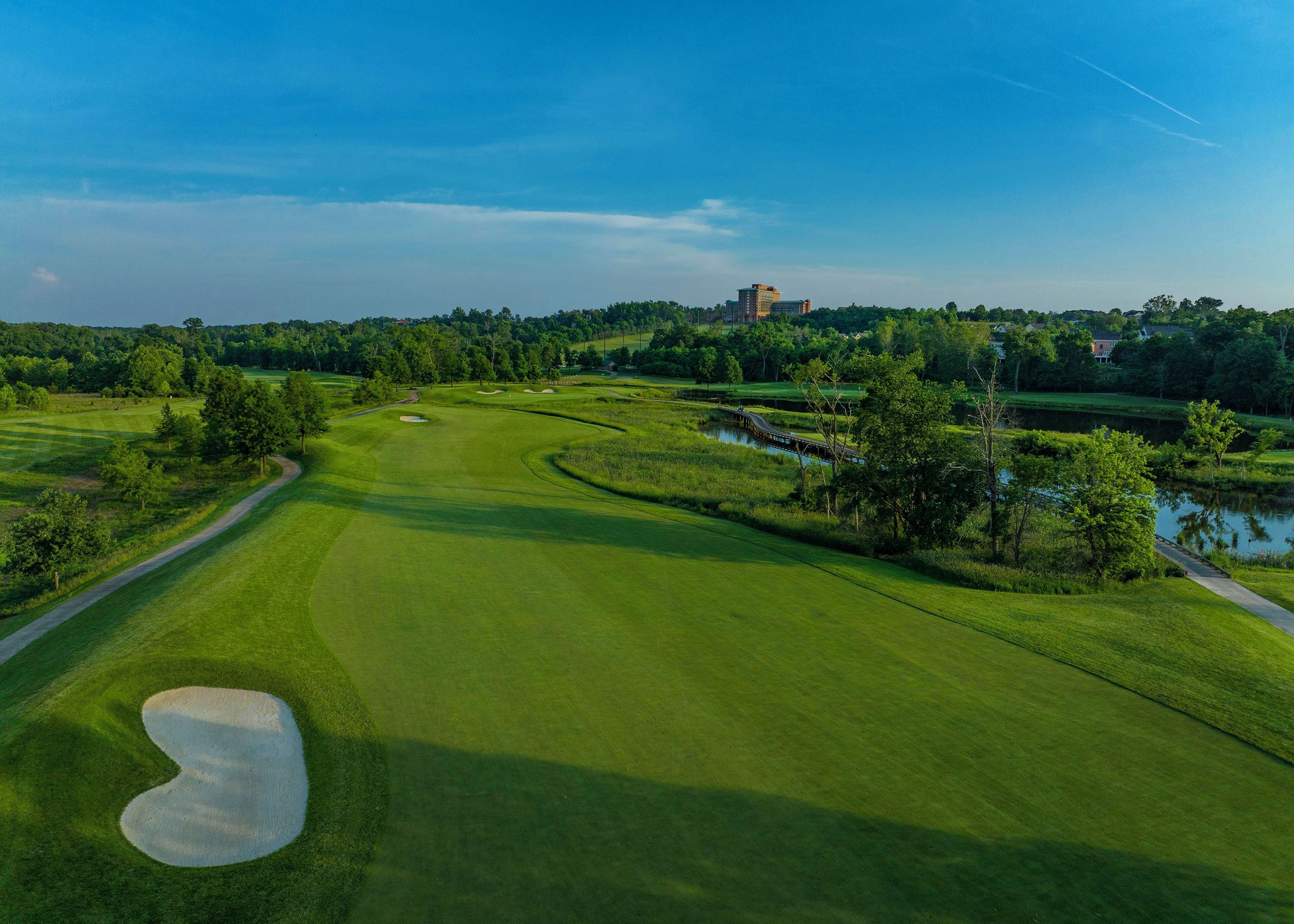 A golf course with a water hazard, a bridge, and a distant building.
