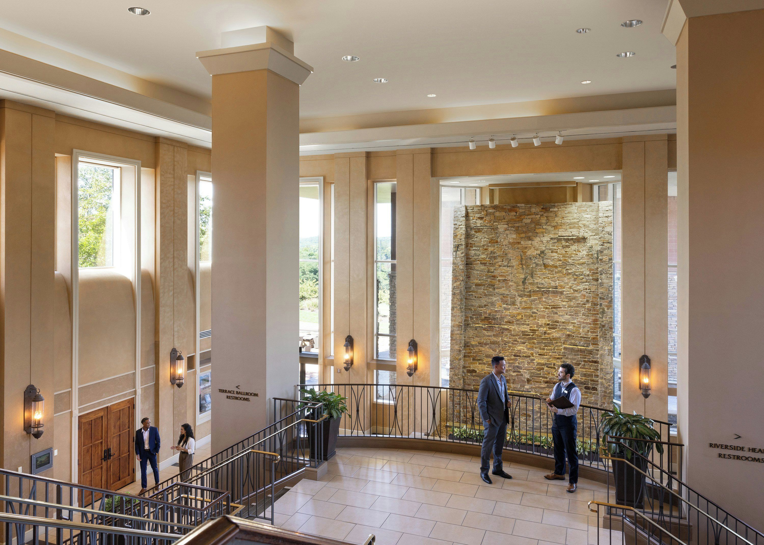 Eine geräumige Lobby mit Steinwand, einer Treppe und einem Schild, das den Standort der Terrasse und der Toiletten angibt.
