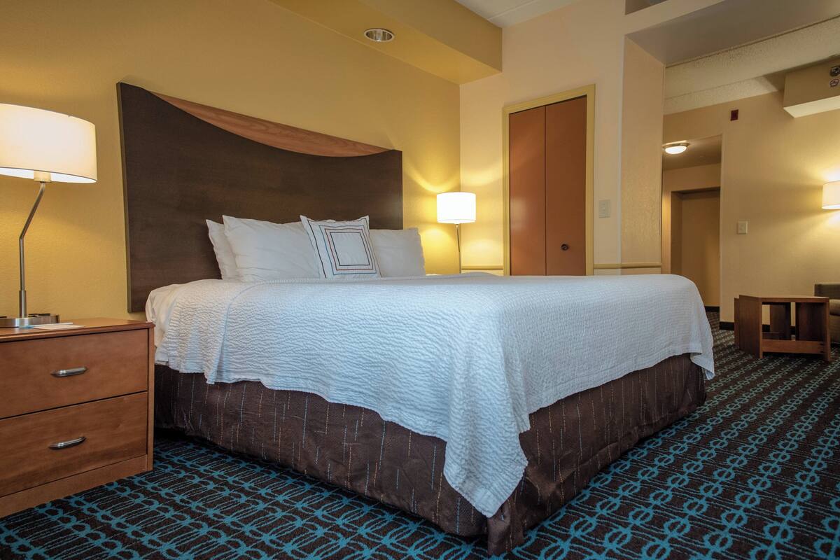 A hotel room with a large bed, a nightstand, a lamp, and a patterned carpet.