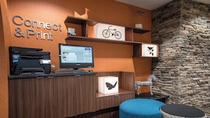 A reception area with a wooden desk, a computer, a printer, and a sign that reads "Connect & Print". There are shelves with decorative items and a stone wall in the background. - Fairfield Inn & Suites by Marriott Knoxville/East (Knoxville)