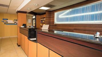A reception area with a wooden reception desk, a computer, and a window with blinds.