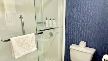 Un baño moderno con ducha de mampara de vidrio, inodoro y repisa de vidrio con artículos de aseo.