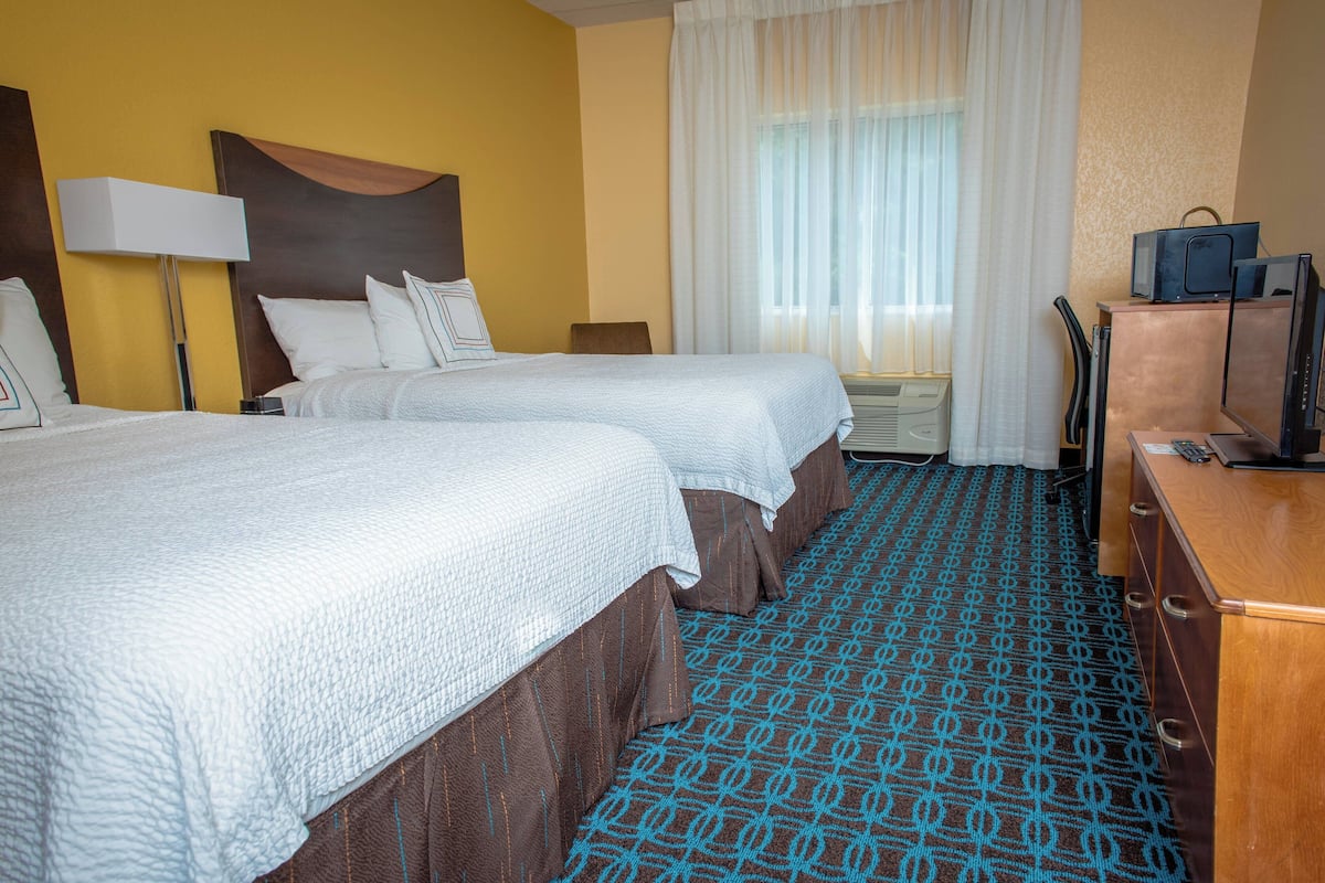 A hotel room with two beds, a desk, a lamp, a television, and a window with curtains.
