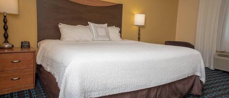 Habitación de hotel con una cama grande, una mesita de noche de madera con una lámpara, una silla y un calentador de pared.