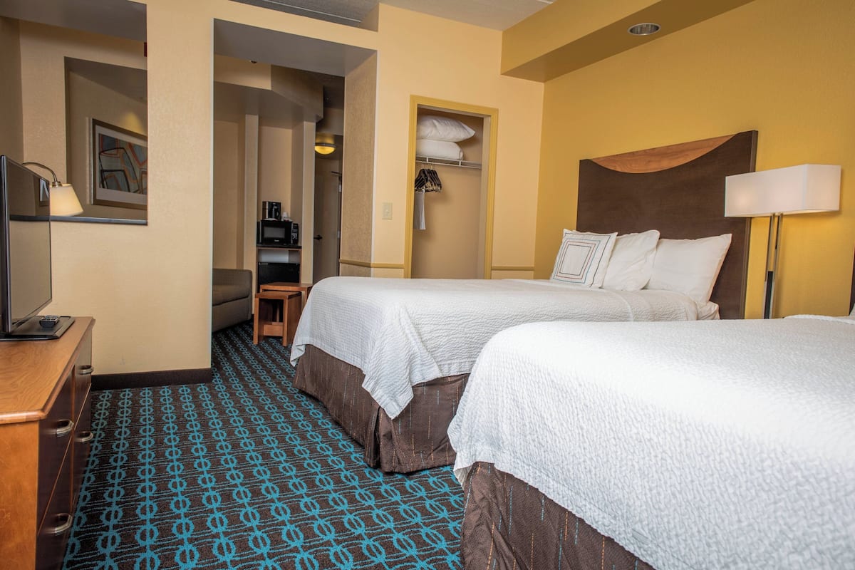 A hotel room with two beds, a desk, and a bathroom visible through an open door.