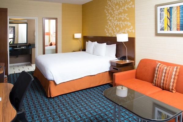 A hotel room with a bed, a sofa, a table, a desk, and a mirror.