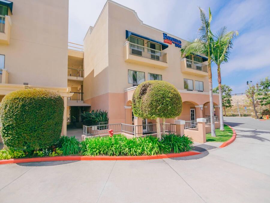 A Faber Inn hotel with a modern design, featuring a flat roof, large windows, and a well-maintained garden with neatly trimmed bushes and a palm tree.