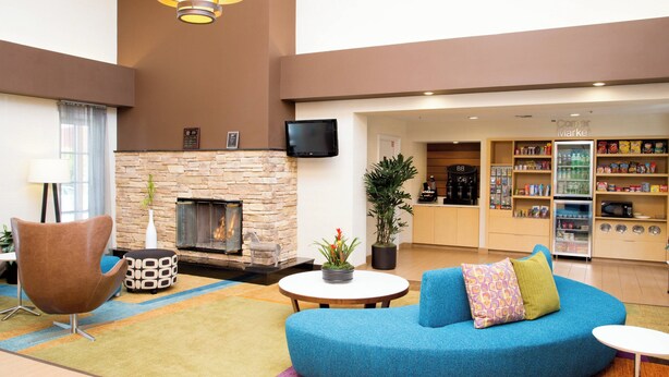 A modern lobby with a stone fireplace, a flat-screen TV, a seating area with a blue sofa, and a kitchenette in the background. - Fairfield Inn by Marriott Anaheim Hills Orange County (Anaheim)